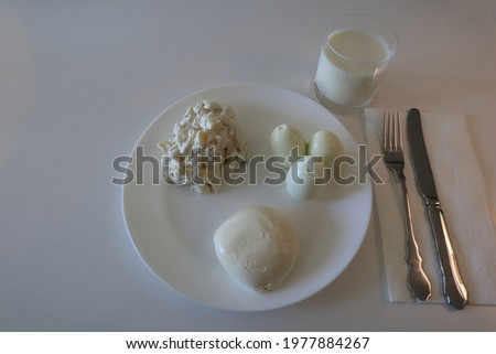Lunch or dinner in only white color. Potato salad, mozzarella cheese, boiled eggs and milk to drink. Inside or indoor photo. Napkin under cutlery. Copy space for text. Stockholm, Sweden.