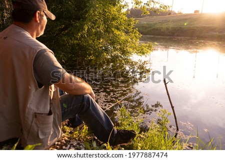 50+ age fisherman sitting in front of the pond on a sunset with simple fishing rod, man relaxing while fishing in the evening, soft sun light