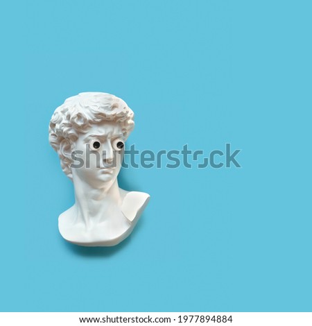 Plaster sculpture head of David with google eyes. Gypsum copy of antique statue on blue background. modern style. creative minimal art concept. flat lay. copy space Royalty-Free Stock Photo #1977894884