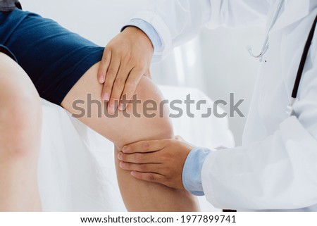 Doctor physiotherapist working examining treating injured knee of patient, his using the handle to the patient knee to check for pain. Royalty-Free Stock Photo #1977899741