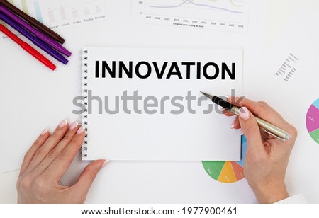 A girl with two hands holds a notebook with the text INNOVATION above a table with diagrams, next to pencils.