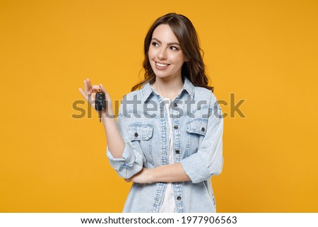 Young smiling dreamful pensive wistful happy rich brunette woman 20s wearing stylish denim shirt white t-shirt holding in hands car keys look aside isolated on yellow color background studio portrait Royalty-Free Stock Photo #1977906563