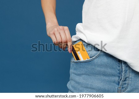 Close up cropped photo portrait shot of caucasian female hand arm putting credit bank card in jeans pants denim pocket isolated on dark blue background studio portrait. Money finance currency concept Royalty-Free Stock Photo #1977906605