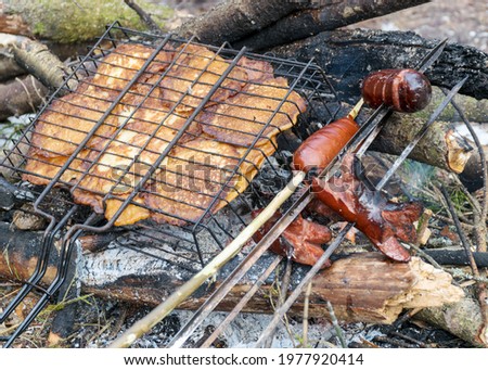 picture with snowy background and picnic accessories, campfire and iron skewers with sausages and pancakes for baking on the campfire in winter, tourist lunch by the nature in winter
