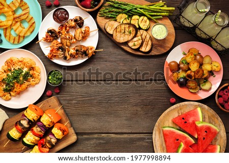 Healthy plant based summer bbq arch frame. Overhead view on a dark wood background. Grilled fruit and vegetables, skewers, cauliflower steak and vegetarian sides. Copy space. Meat substitute concept.