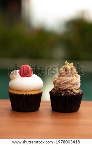 Cupcake, one with vanilla cream and a franboesa, the other with nut chocolate. Vertical images. Blurred background.