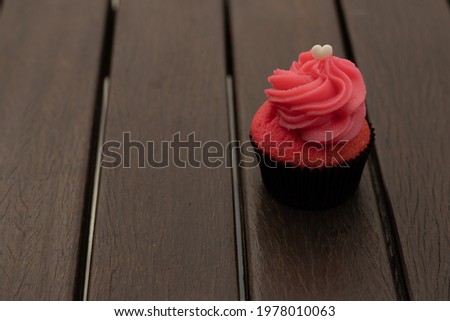 Small tasty cupcake on a dark ripped wooden table. Horizotal image with cupcake on the side leaving space for text. Blurred background.