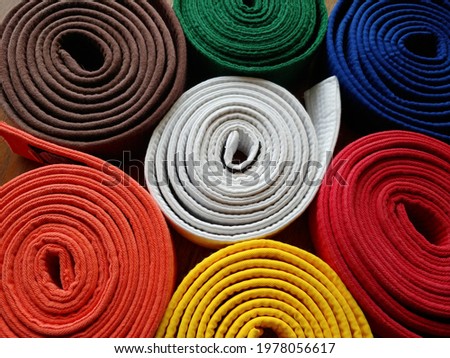 Close up top view, looking down at brightly coloured coiled (rolled) karate belts, martial arts, white, yellow, orange, red, green, blue, brown, status and kyu rank Royalty-Free Stock Photo #1978056617