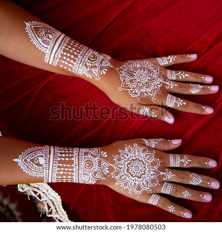 White bridal henna tattoos on two hands on red background. Moroccan wedding preparation henna party. Temperate white mehndi. Modern mehendi art.