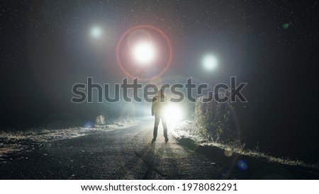 UFO concept. Glowing orbs, floating above a misty road at night. With a silhouetted figure looking at the lights.                Royalty-Free Stock Photo #1978082291