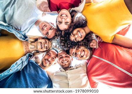 Multiracial group of young people standing in circle and smiling at camera - Happy diverse friends having fun hugging together - Low angle view Royalty-Free Stock Photo #1978099010