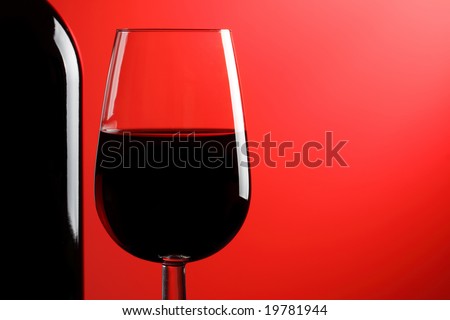 A glass of red wine and bottle on a red background.