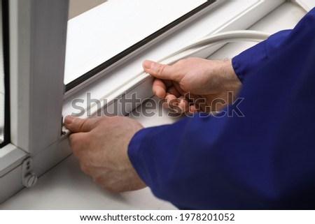 Worker putting rubber draught strip onto window indoors, closeup Royalty-Free Stock Photo #1978201052