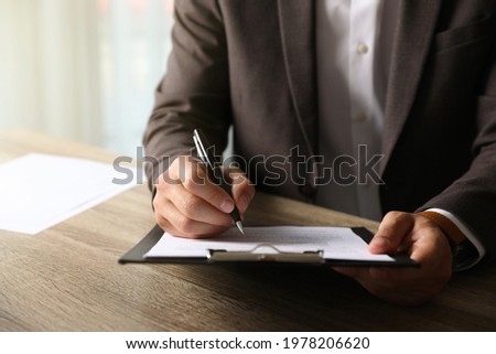 Businessman signing document at table indoors, closeup