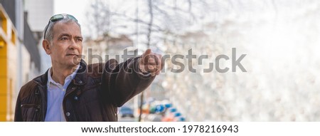 Elegant mature man walking on an urban sidewalk and pointing a direction