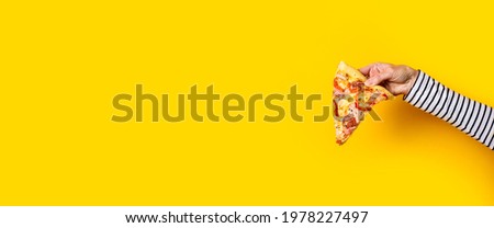 female hand holds a slice of fresh hot pizza on a yellow background. Banner.