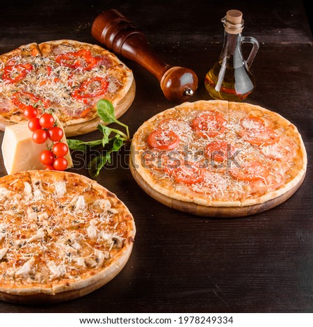 Pizza with chicken, mushrooms, cheese, sauce, ham, salami, pepper, tomatoes on a dark wooden table. Assortment of pizzas