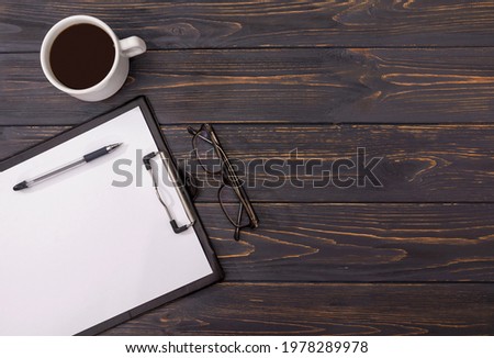 tablet with a white sheet, glasses, a pen and a cup of coffee on a wooden background with boards. View from above. Copy space.
