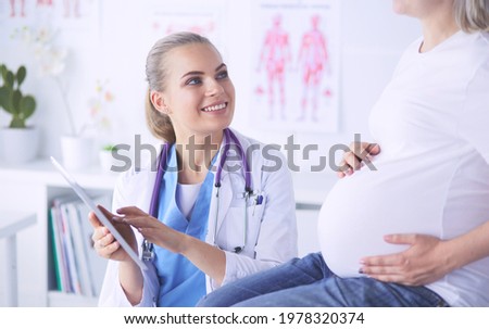 Smiling woman doctor shows pictures on the tablet to pregnant young woman at hospital.