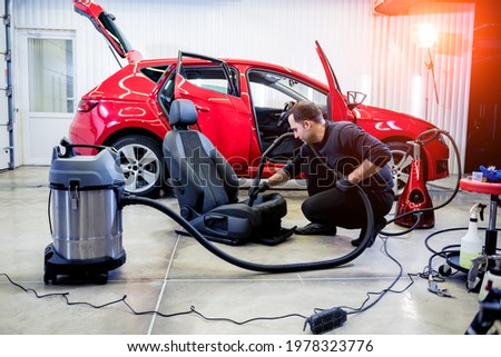 Car service worker cleaning car seat with vacuum cleaner. Royalty-Free Stock Photo #1978323776