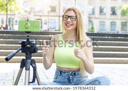 Like it. Young happy woman blogger recording video on smartphone while sitting on the steps near the university. Thumb up. 