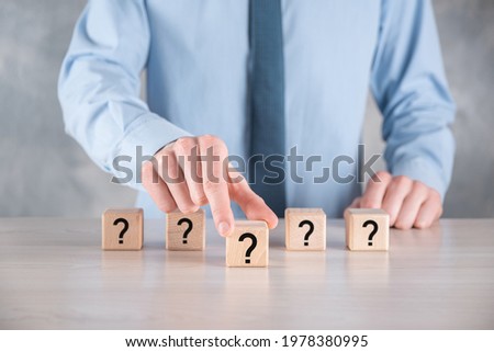Businessman hold and put wooden cube block shape with question marks on grey table. Space for text.concept for confusion, question or solution.