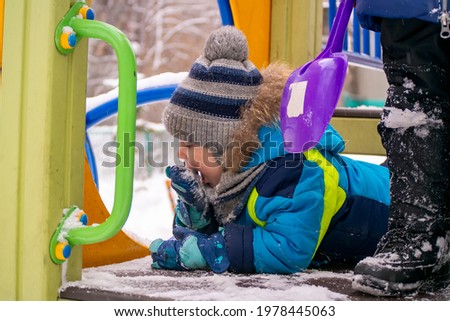 a little boy eats snow from a mitt in winter
