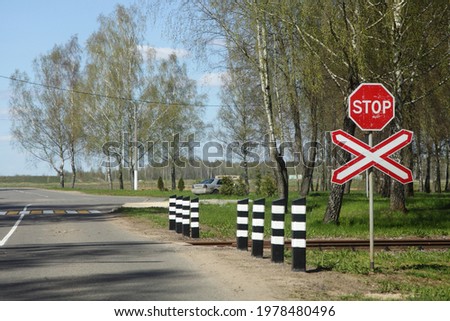 Road sign STOP on suburban non regulated empty one way railroad crossing on asphalted road view from car, beautiful European railway landscape at Sunny summer day on blue sky and birch tree background Royalty-Free Stock Photo #1978480496