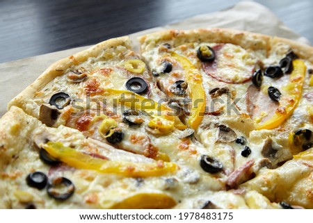 Pizza with chesse, ham, yellow bell pepper, olives and mushrooms. Sliced pizza on wooden table, closeup