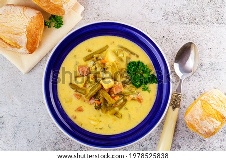 Creamy vegetable soup made from cut green beans, carrot, potato and pieces of ham.