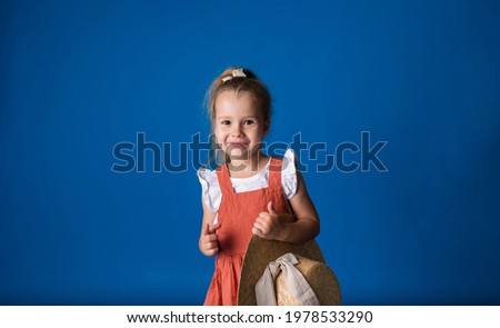 a smiling little girl with a straw hat stands and looks at the camera on a blue background with space for text. Summer background