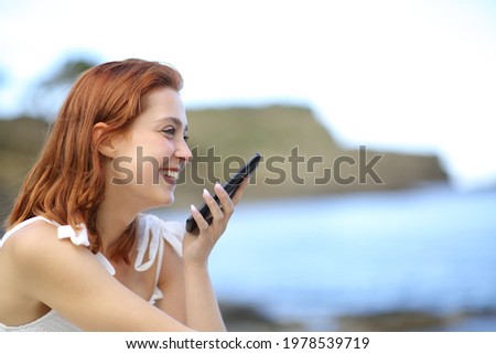 Happy woman using voice recognition on smart phone sitting on the beach