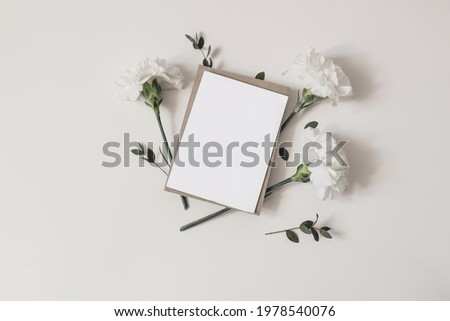Feminine  wedding, birthday stationery composition. Blank greeting card, invitation mockup with craft envelope. White carnation flowers and eucalyptus branches isolated on table background. Flat lay, 