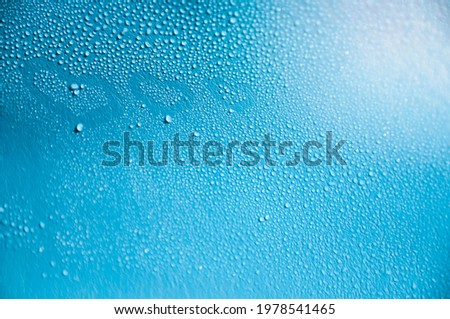 Blue background with water drops and drawn 3 hearts on wet glass with selective focus and highlights in the upper corner of the photo.