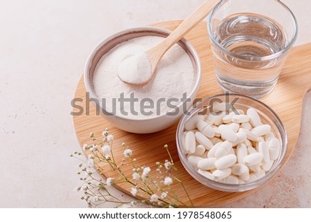 Collagen powder, pills and glass of water on wooden tray, top view Royalty-Free Stock Photo #1978548065
