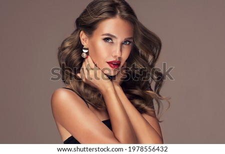 Beautiful smiling woman with long wavy hair .  Girl curly hairstyle  and red manicure nails . Beauty ,makeup and cosmetics . Earring jewelry
