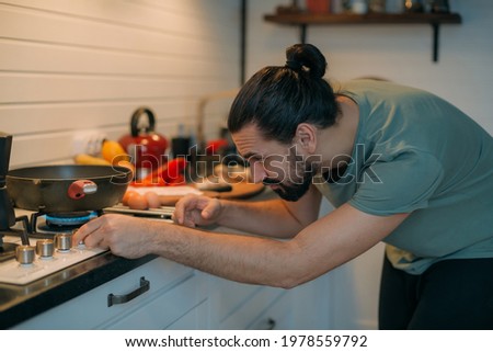 A man prepares breakfast in the kitchen. Young handsome caucasian male preparing food for himself for lunch on a gas stove in a large bright kitchen Royalty-Free Stock Photo #1978559792