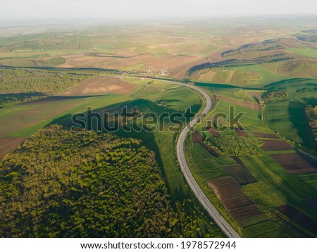 Aerial Drone View Flight over forest and asphalt road in sunset soft light. Cinematic drone shot flying over country road with curved.