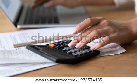 Close up young woman using calculator, managing household budget, counting paper bills or taxes, managing monthly budget, doing financial paperwork alone at home, accounting bookkeeping concept. Royalty-Free Stock Photo #1978574135