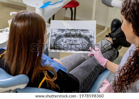Dentist explaining the details of a x-ray teeth picture to his patient in clinic. Oral care, orthodontics.