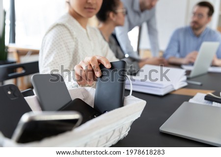 Close up Indian businesswoman putting phone in basket, employee entrepreneur woman sitting at table in boardroom, involved in briefing, meeting, no cellphone zone in office or digital detox concept Royalty-Free Stock Photo #1978618283