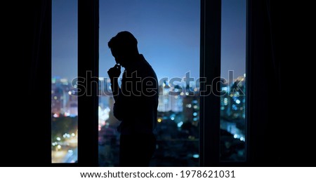 worried asian young businessman is standing near windows while working overtime in office at night Royalty-Free Stock Photo #1978621031