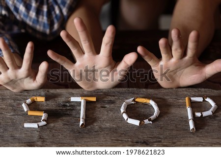 Word stop spelled using cigarettes on wooden background with stop hands