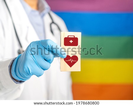 A doctor hand holding wooden blocks with icons of health against the background of the rainbow flag (LGBT). Close-up photo. Space for text. Medical and healthcare concept.