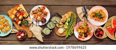 Healthy plant based summer bbq table scene. Overhead view on a dark wood banner background. Grilled fruit and vegetables, skewers, cauliflower steak and vegetarian sides. Meat substitute concept.