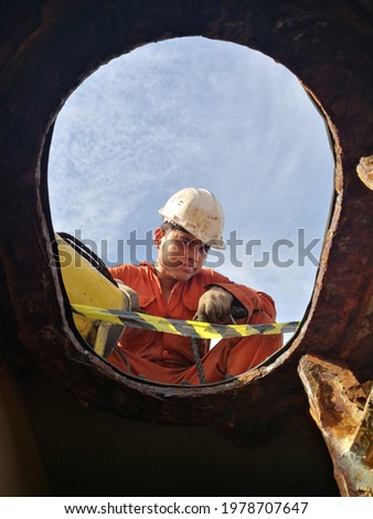 a seaman is standing by on top of the enclosed space or tank entrance of a ship. Royalty-Free Stock Photo #1978707647