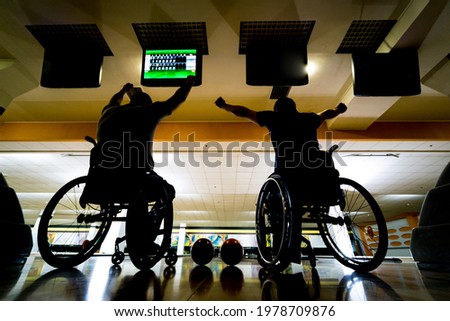 Two young disabled men in wheelchairs playing bowling in the club
