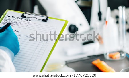 Food safety and quality management. Food safety and quality inspector filling out quality control form in a laboratory, salmon in background Royalty-Free Stock Photo #1978725320
