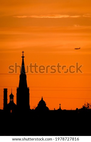 Conceptual photo of city downtown at sunset with skyline silhouette against a beautiful orange sky a airplane. Defocused