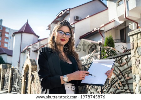 portrait of a realtor woman standing in front of a new house. sale or rent concept